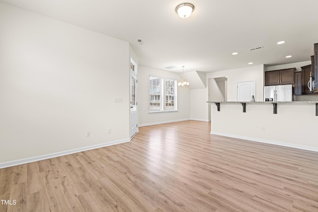 unfurnished living room with a chandelier and light wood-type flooring