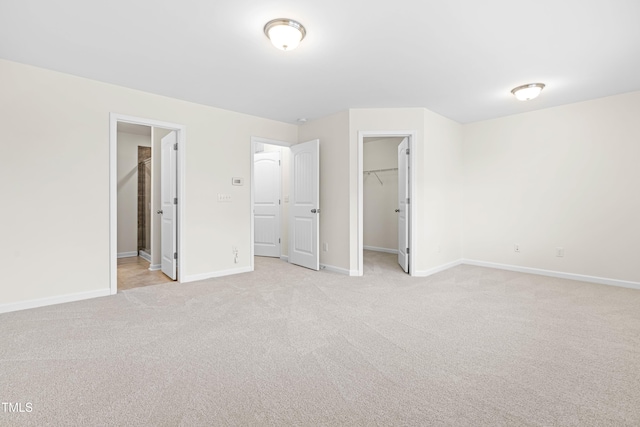 unfurnished bedroom with ensuite bath, light colored carpet, a closet, and a spacious closet