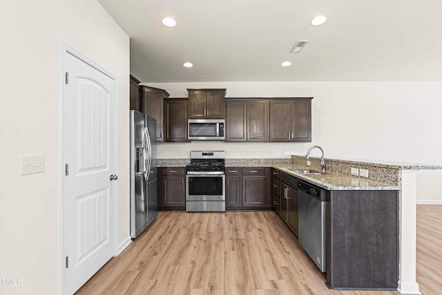 kitchen with kitchen peninsula, stainless steel appliances, light stone countertops, dark brown cabinetry, and sink