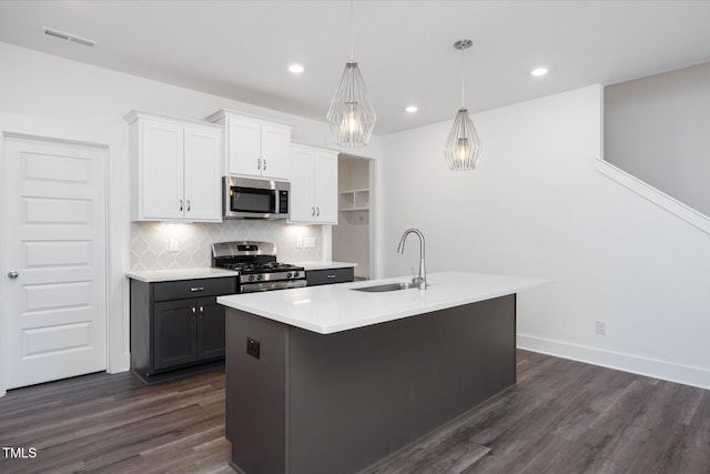 kitchen featuring pendant lighting, sink, stainless steel appliances, white cabinets, and a center island with sink