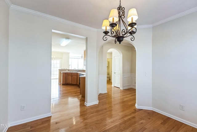 unfurnished dining area featuring light hardwood / wood-style floors, sink, ornamental molding, and an inviting chandelier