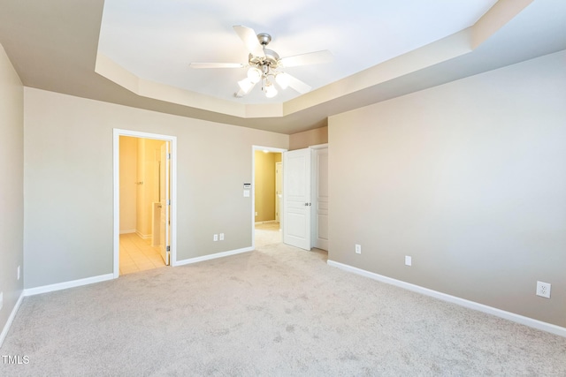 unfurnished bedroom with connected bathroom, ceiling fan, a raised ceiling, and light carpet