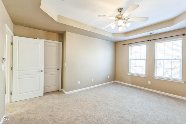 unfurnished bedroom featuring ceiling fan, a tray ceiling, a closet, and light carpet