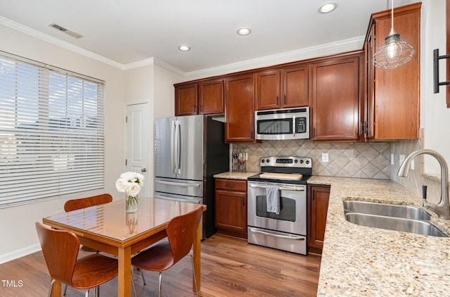 kitchen with appliances with stainless steel finishes, decorative light fixtures, sink, ornamental molding, and light stone counters