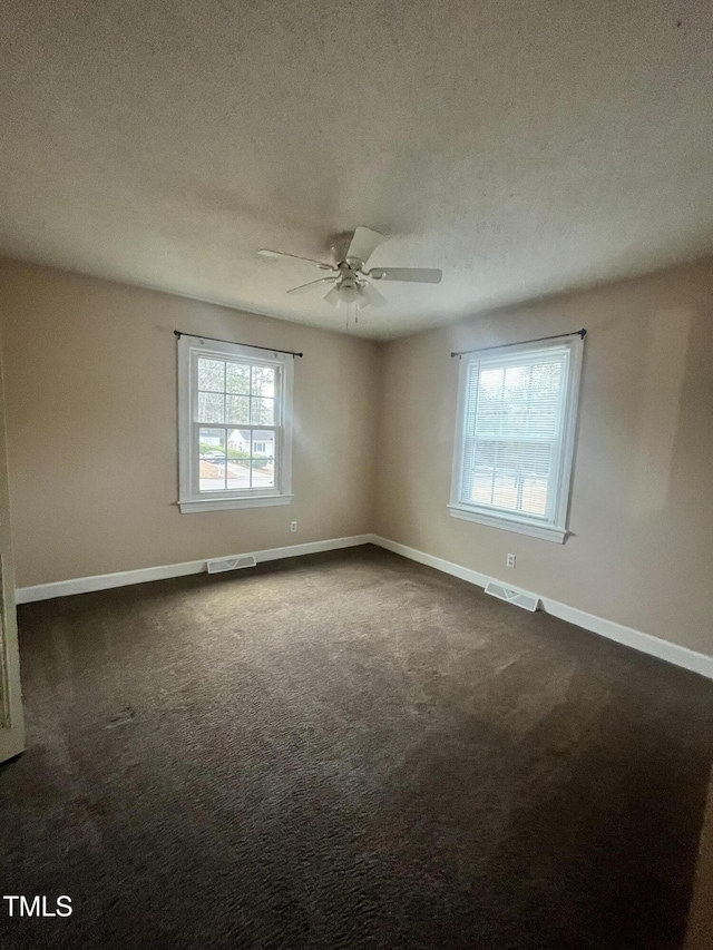 unfurnished room featuring a textured ceiling, dark colored carpet, and a healthy amount of sunlight