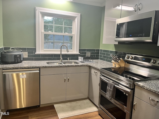 kitchen with stainless steel appliances, decorative backsplash, white cabinets, light stone counters, and sink