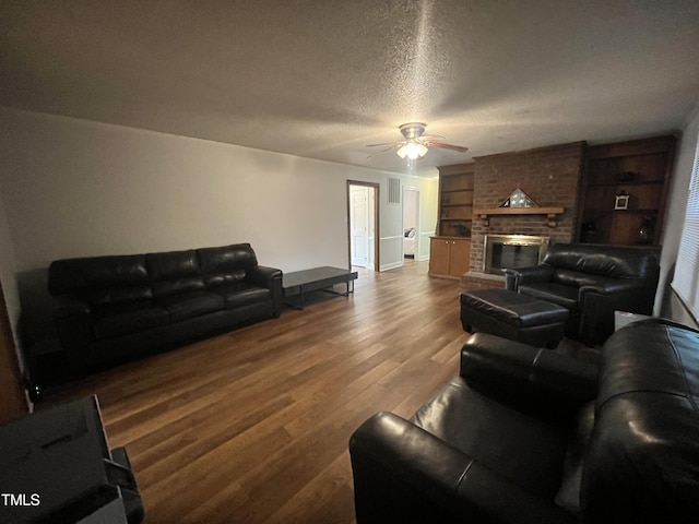 living room with ceiling fan, a fireplace, wood-type flooring, a textured ceiling, and built in shelves