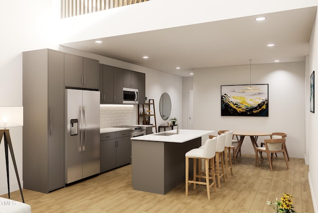 kitchen featuring appliances with stainless steel finishes, tasteful backsplash, light wood-type flooring, sink, and a breakfast bar area