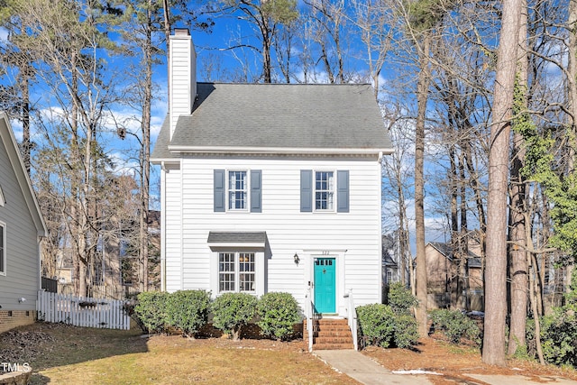 view of front of house featuring a front yard, a chimney, fence, and roof with shingles