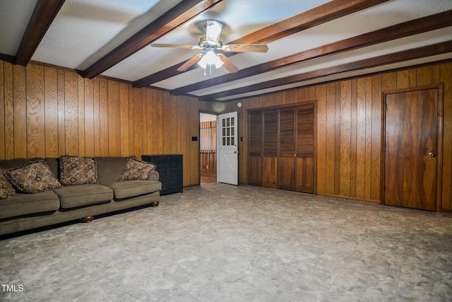 living room featuring ceiling fan, beam ceiling, and wood walls