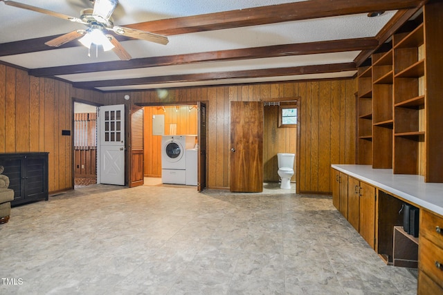 unfurnished living room with ceiling fan, washing machine and dryer, beamed ceiling, and wood walls