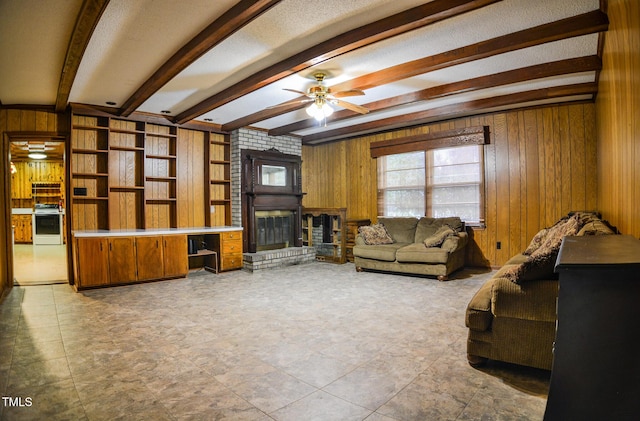 living room featuring ceiling fan, wood walls, beamed ceiling, and a fireplace