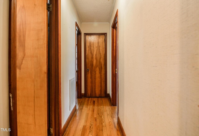 corridor with light wood-type flooring and a textured ceiling