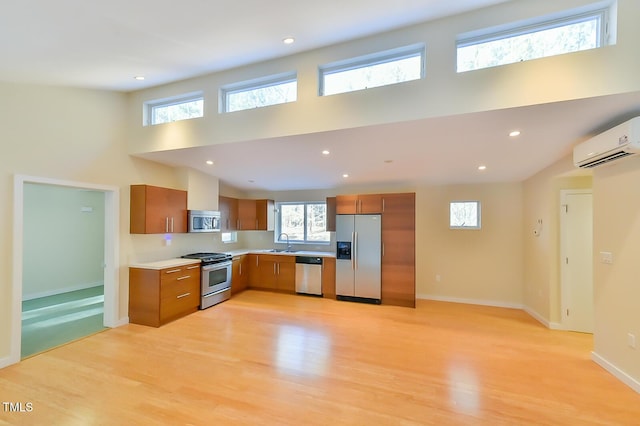 kitchen with light hardwood / wood-style flooring, a wall unit AC, sink, a towering ceiling, and stainless steel appliances