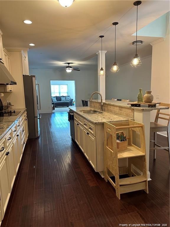 kitchen featuring a center island with sink, decorative light fixtures, stainless steel refrigerator, a breakfast bar, and sink