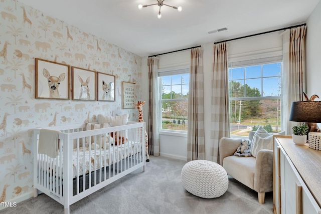 carpeted bedroom featuring a nursery area and an inviting chandelier