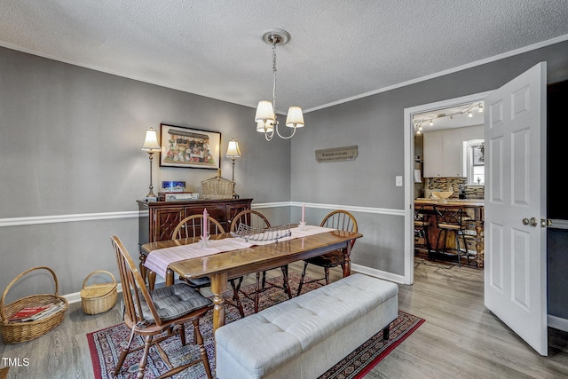 dining room featuring light hardwood / wood-style flooring, crown molding, an inviting chandelier, and a textured ceiling