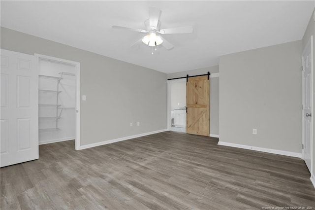 unfurnished bedroom with a spacious closet, hardwood / wood-style floors, a closet, ceiling fan, and a barn door