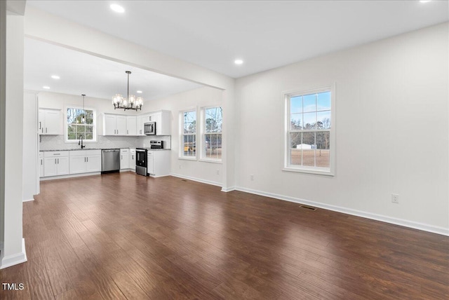 unfurnished living room featuring dark hardwood / wood-style floors, sink, and an inviting chandelier