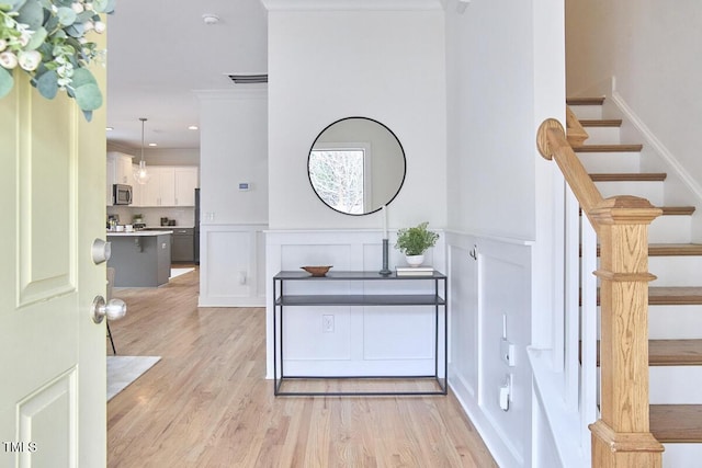 entrance foyer with light wood-style flooring, a wainscoted wall, visible vents, stairway, and crown molding