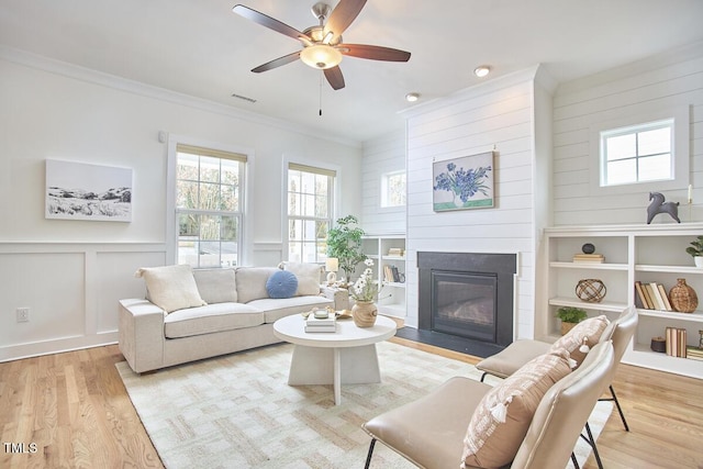 living area with ornamental molding, a fireplace with flush hearth, a decorative wall, and light wood finished floors