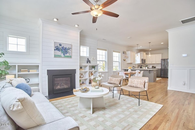 living room with light wood finished floors, visible vents, a decorative wall, ornamental molding, and a large fireplace