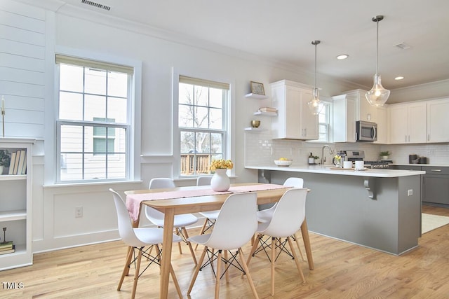 kitchen featuring stainless steel appliances, backsplash, ornamental molding, and light wood-style flooring