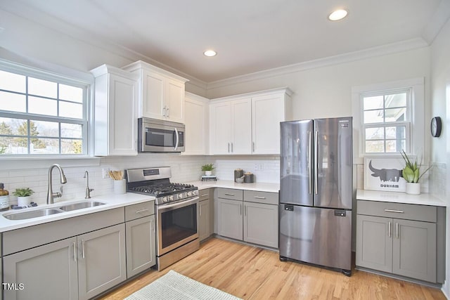 kitchen with a sink, light wood-style floors, ornamental molding, appliances with stainless steel finishes, and gray cabinets