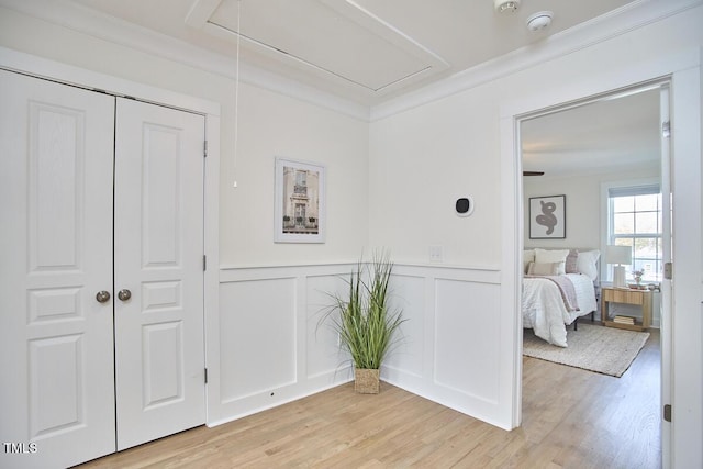 bedroom featuring attic access, light wood-type flooring, and ornamental molding