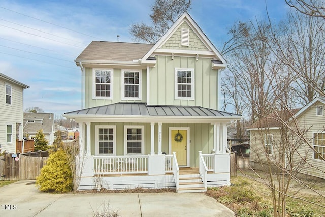 view of front of house featuring covered porch, board and batten siding, a standing seam roof, fence, and metal roof