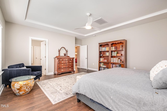 bedroom featuring ceiling fan, ensuite bathroom, dark hardwood / wood-style flooring, and a raised ceiling