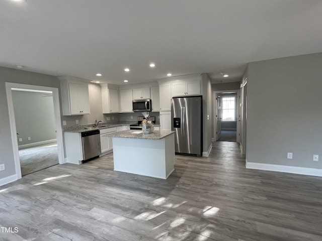 kitchen with light stone countertops, appliances with stainless steel finishes, white cabinetry, and a center island