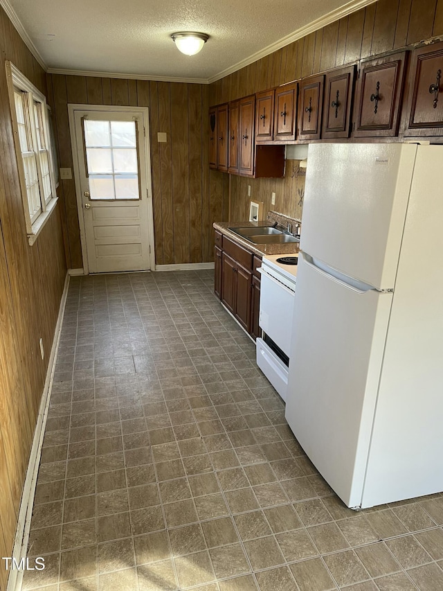 kitchen with sink, crown molding, white appliances, wooden walls, and a textured ceiling