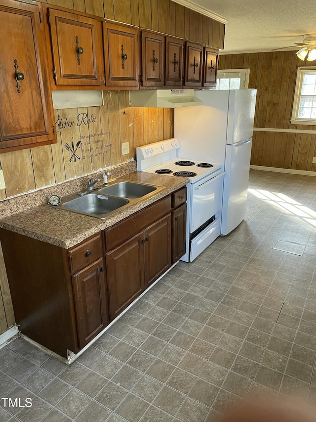 kitchen with sink, wood walls, white appliances, a textured ceiling, and ceiling fan