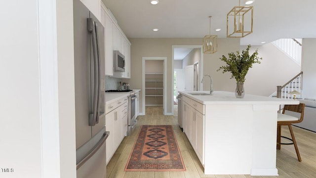 kitchen with pendant lighting, white cabinets, appliances with stainless steel finishes, sink, and a kitchen island with sink