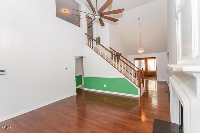 unfurnished living room featuring dark wood-type flooring, ceiling fan, and a towering ceiling