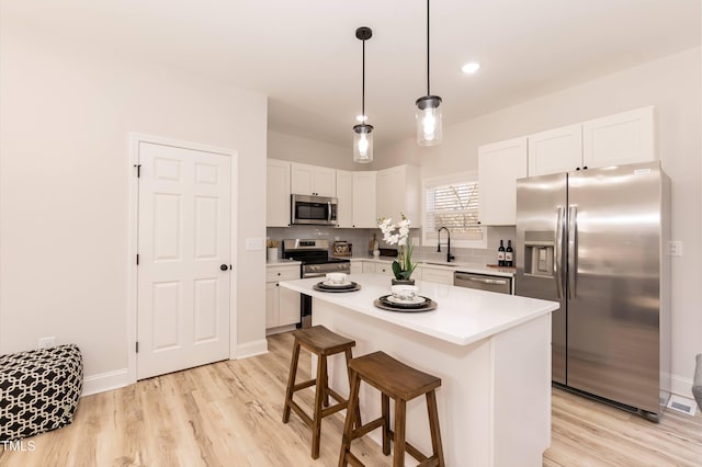 kitchen with white cabinetry, appliances with stainless steel finishes, tasteful backsplash, hanging light fixtures, and a kitchen island