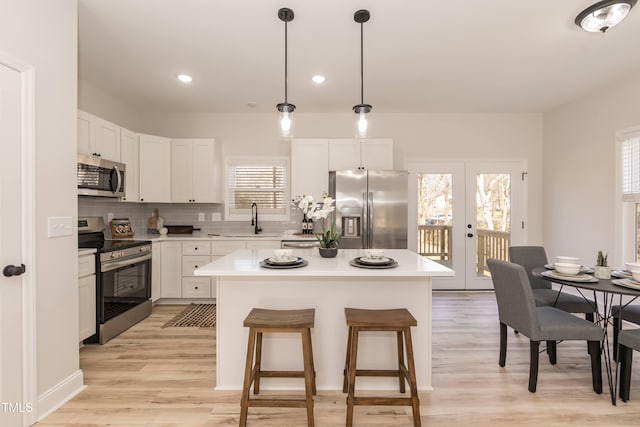 kitchen featuring appliances with stainless steel finishes, a kitchen island, decorative light fixtures, white cabinetry, and french doors