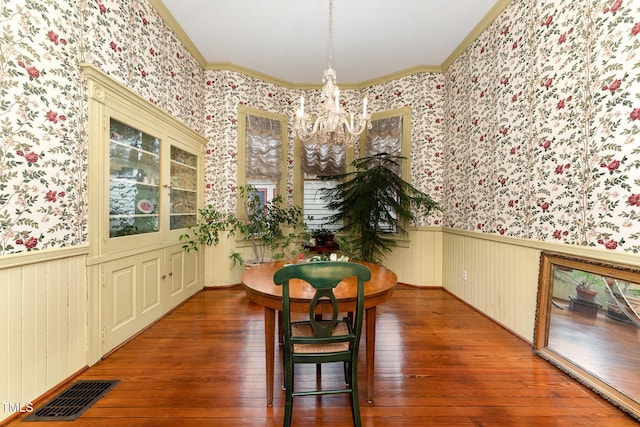 dining area with dark wood-type flooring, ornamental molding, and a notable chandelier