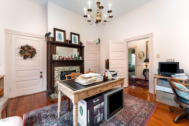 home office featuring wood-type flooring, a stone fireplace, and a chandelier