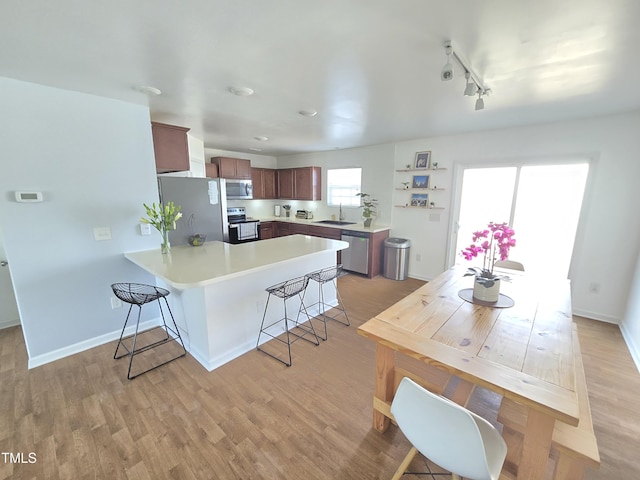 kitchen with appliances with stainless steel finishes, sink, a kitchen breakfast bar, kitchen peninsula, and light wood-type flooring