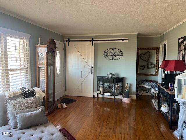 living room featuring a barn door, ornamental molding, a textured ceiling, and hardwood / wood-style floors