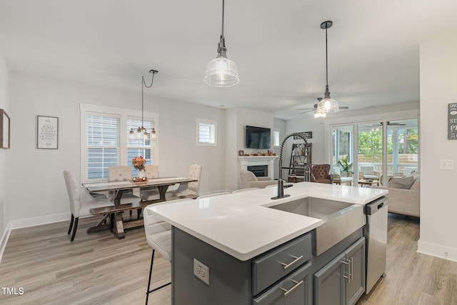 kitchen featuring decorative light fixtures, light hardwood / wood-style flooring, stainless steel dishwasher, and a center island with sink