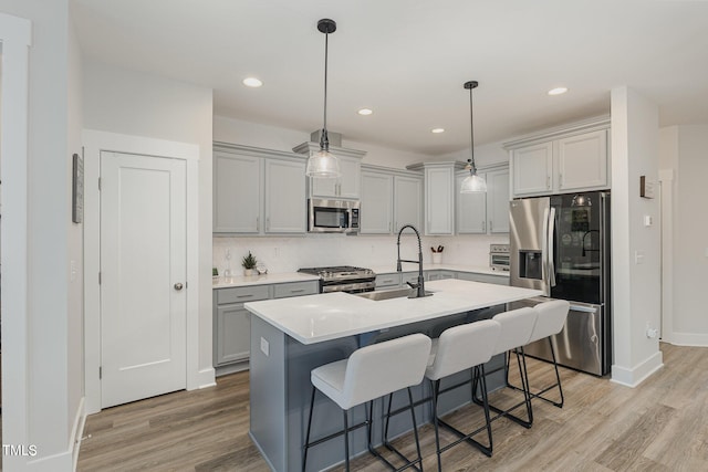 kitchen featuring sink, gray cabinets, an island with sink, pendant lighting, and stainless steel appliances