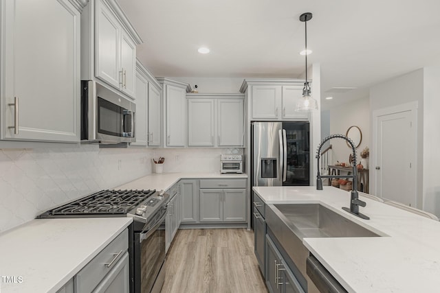 kitchen with pendant lighting, sink, gray cabinets, stainless steel appliances, and light wood-type flooring