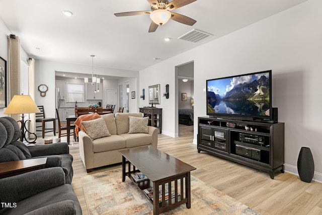 living room with ceiling fan with notable chandelier and light hardwood / wood-style flooring