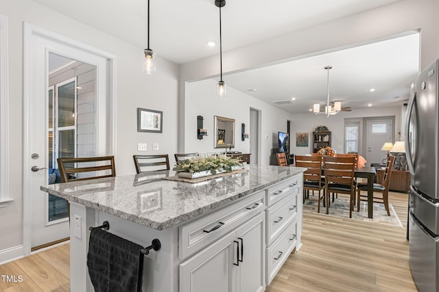 kitchen featuring stainless steel refrigerator, white cabinets, hanging light fixtures, a center island, and light stone counters