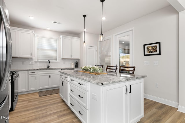 kitchen with light wood-type flooring, stainless steel refrigerator, white cabinets, and a kitchen island