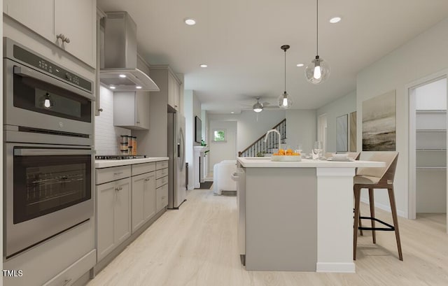 kitchen featuring hanging light fixtures, wall chimney range hood, gray cabinetry, and a breakfast bar area