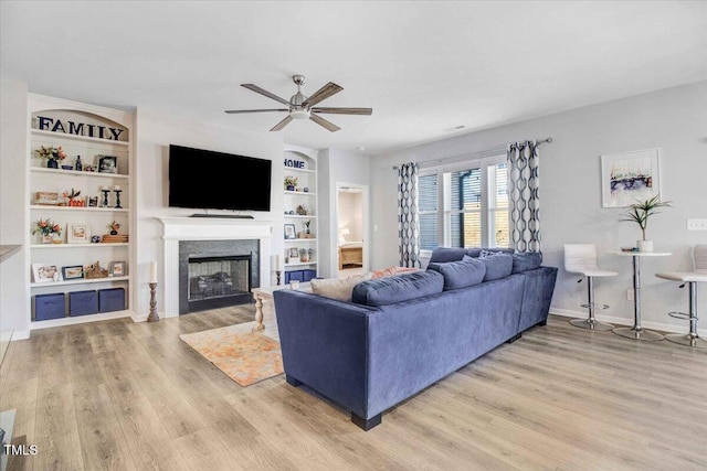 living room with ceiling fan, built in features, and light hardwood / wood-style flooring